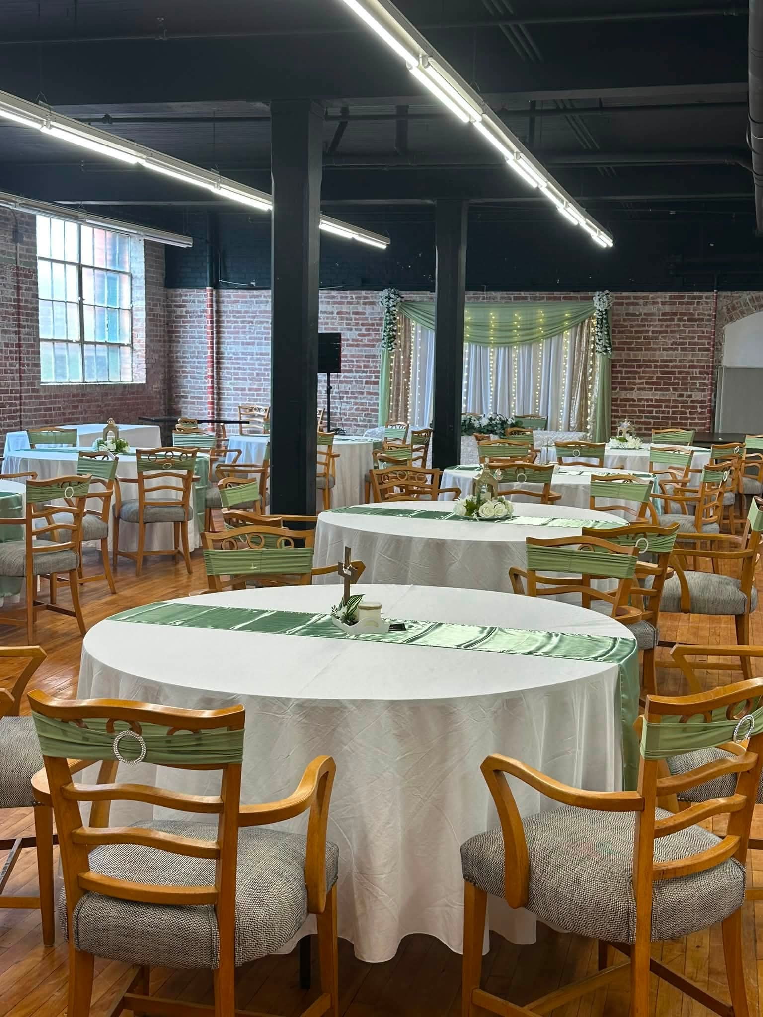 Wedding reception at Pleasant Street Hall with round tables, white linens, sage green satin runners and sashed chairs under exposed brick and black ceiling beams